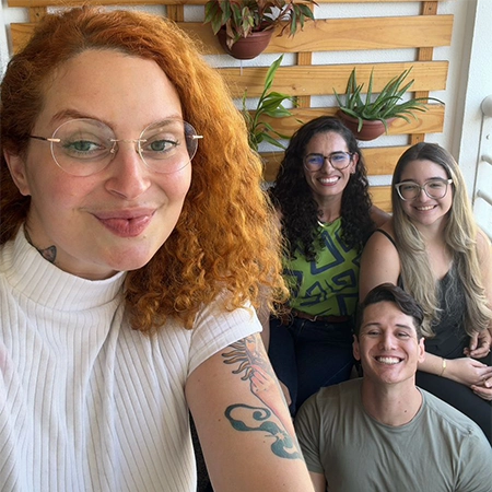 foto da psicóloga Larissa, sorrindo, usando uma camisa de gola rolê branca, com a equipe ao lado, também sorrindo