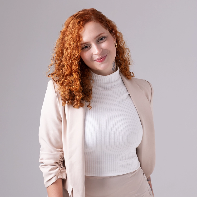 foto da psicóloga Larissa, sorrindo, usando uma camisa de gola rolê branca e um blazer bege